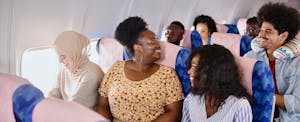 A group of friends laugh with one another as they take their seats on a flight.