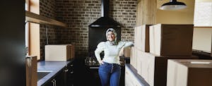 Woman smiling as she stands in her new kitchen surrounded by boxes