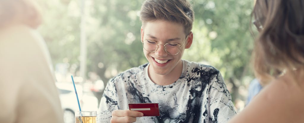 Teenage kid sitting outdoors, smiling at his new debit card