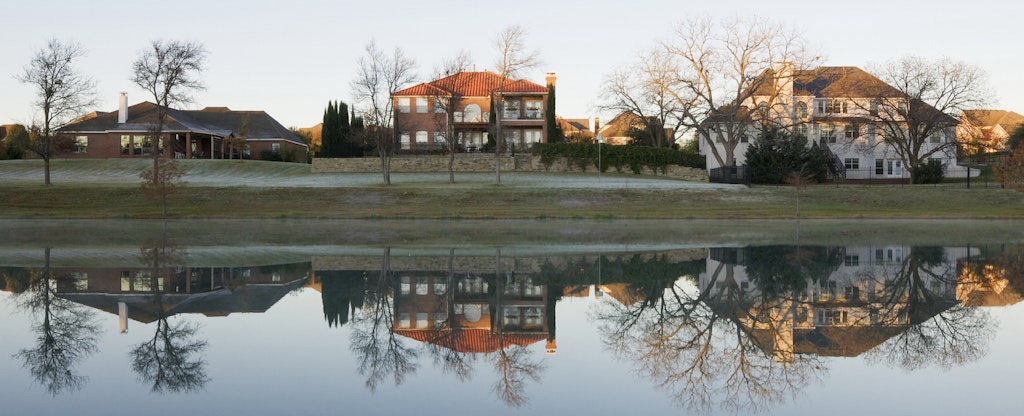 Several two story homes in McKinney, Texas are reflected in the still water of a nearby pond.