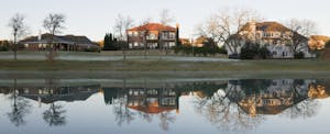 Several two story homes in McKinney, Texas are reflected in the still water of a nearby pond.