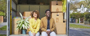Couple sitting together in the bed of their moving truck, smiling as they take a break from moving boxes