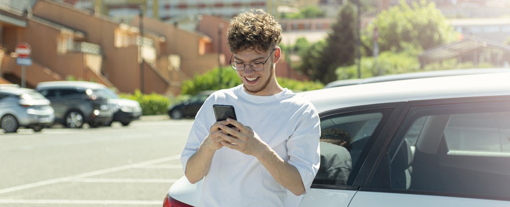 Young man standing next to his car and reading on his phone