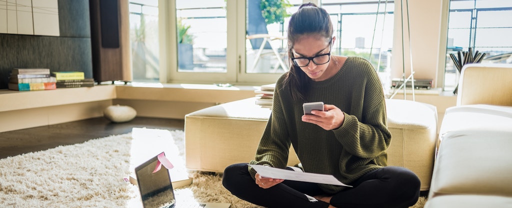 Young woman sitting on the floor of her living room and working.