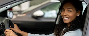Young woman smiling at the camera while behind wheel of her car