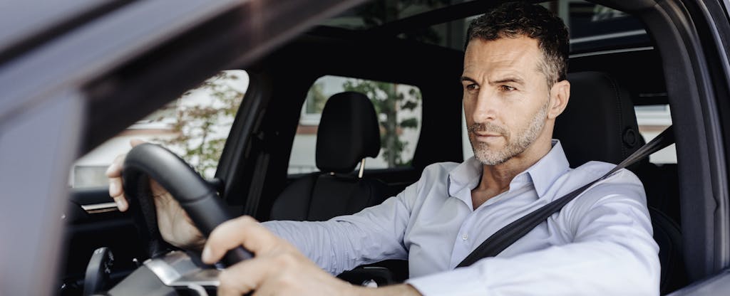A man with a focused expression grasps the steering wheel while sitting in the driver's seat of his car.