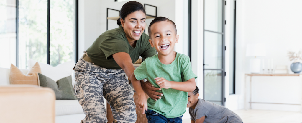 Smiling mom in her military fatigues, chasing after her laughing little boy, in the family living room