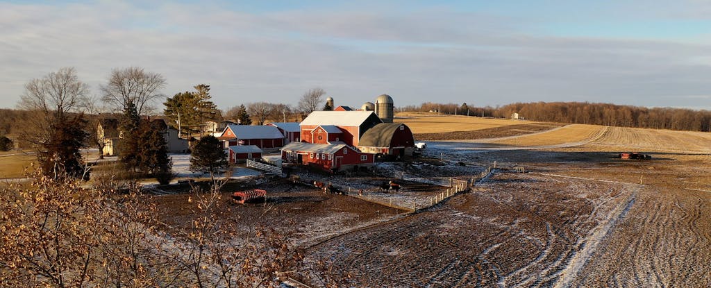 View of fields and a rural farm with a silo on a winter day with snow visible in the ruts of the field.