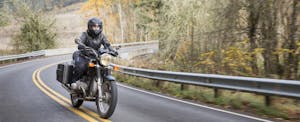 A woman wearing a helmet and protective clothing rides a motorcycle down an empty road in winter.