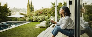 A woman sits on her backyard deck enjoying a glass of wine while taking in the new landscaping she put in using a Figure HELOC.