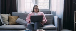 Woman sitting on her couch, reading on her laptop about First Tech Credit Union personal loans