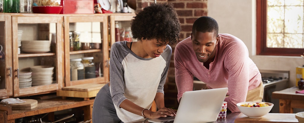 A couple lean over their kitchen island while using a laptop to research HELOCs for investment properties.