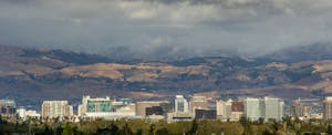 The skyline of San Jose, California under stormy clouds with rolling hills in the background.