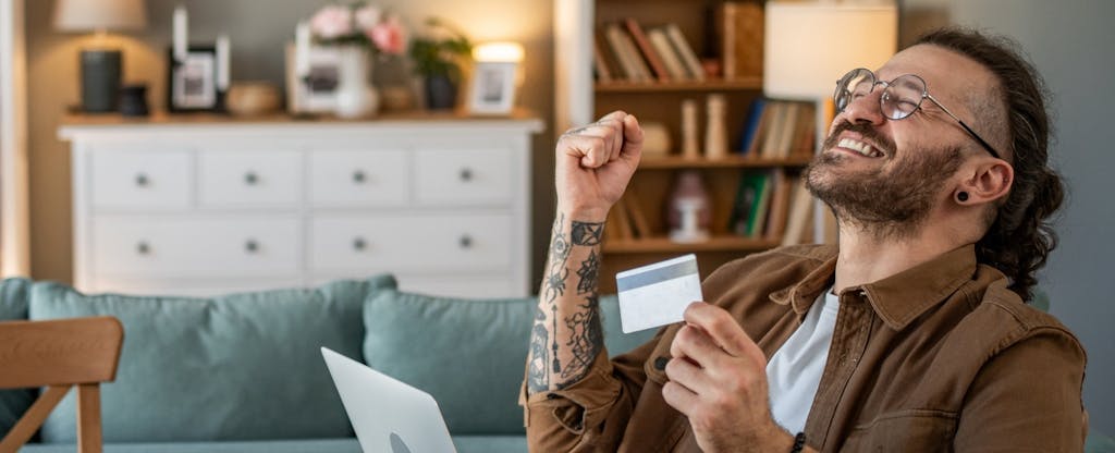 Man ecstatic, holding his credit card while on his laptop.