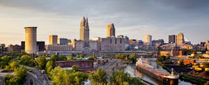 The downtown Cleveland skyline at dusk with the Cuyahoga River in the foreground.