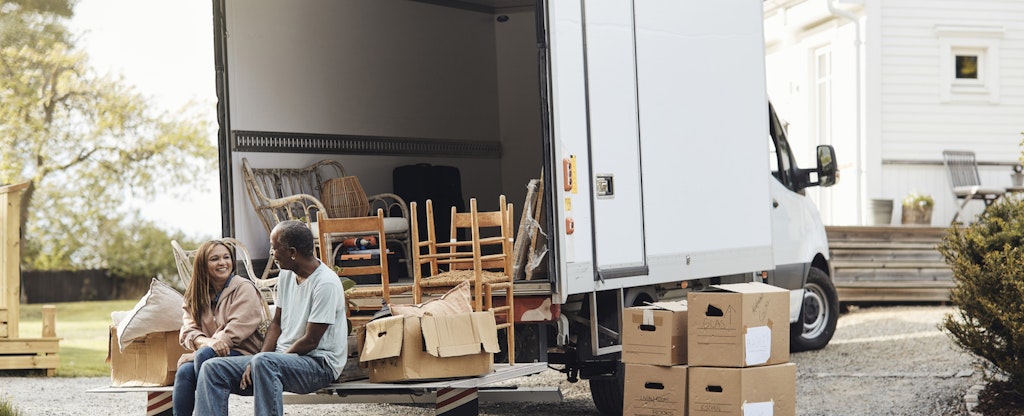 Couple talking to each other while sitting by cardboard boxes near van