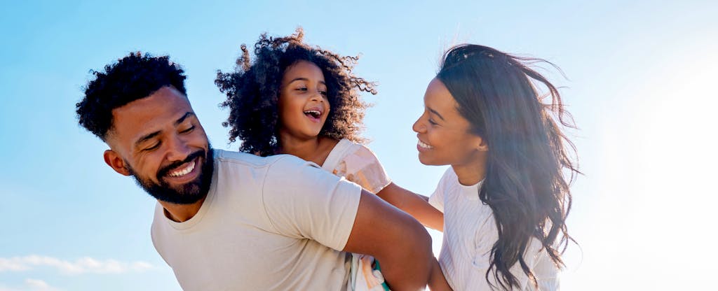 Closeup of a young black couple with their small child, laughing in the sunshine on the beach
