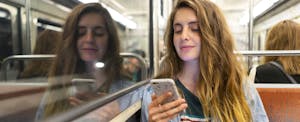 A young woman riding an underground train uses her smartphone to read about getting car insurance without a license.