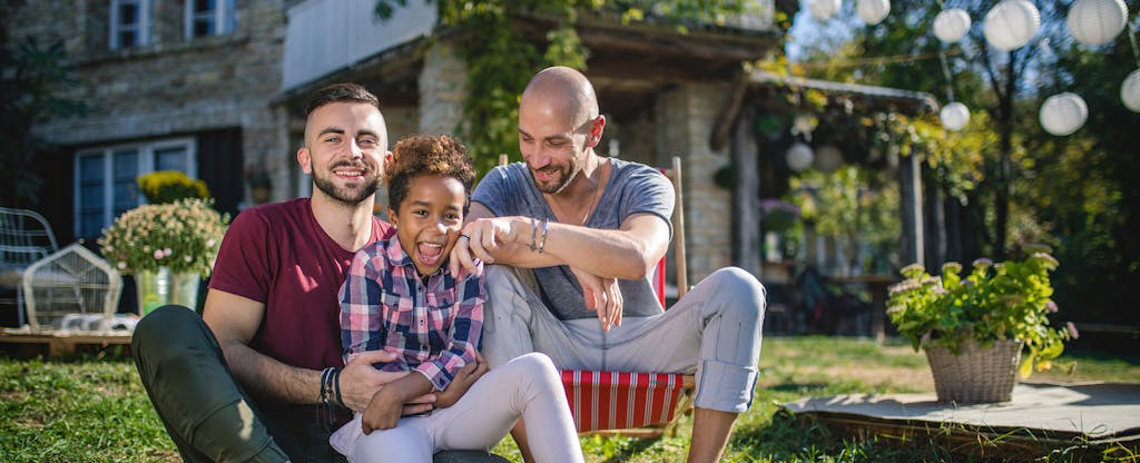 Loving gay parents playing with their child in the front yard of their home.
