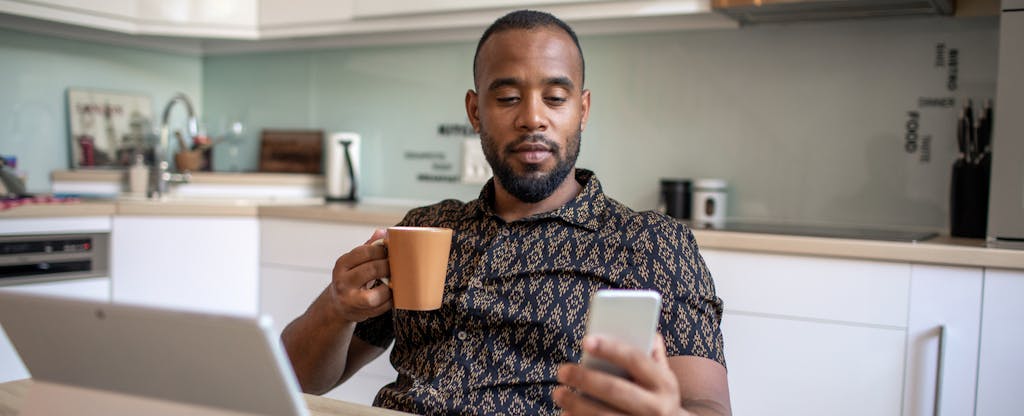 A person drinking coffee in their kitchen uses their smartphone and tablet to research how to take equity out of your home.