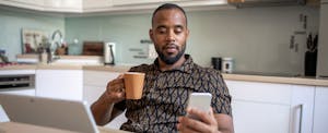 A person drinking coffee in their kitchen uses their smartphone and tablet to research how to take equity out of your home.