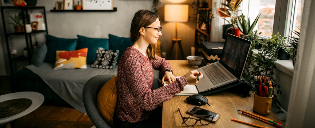 Young woman at home in her living room, at her desk, taking a meeting from her laptop