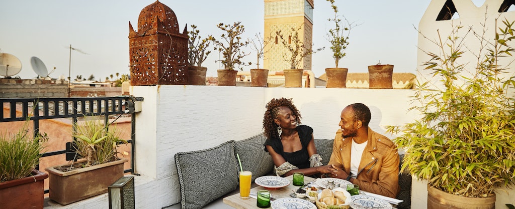 Couple smiling at each other as they sit together at a rooftop restaurant while on vacation
