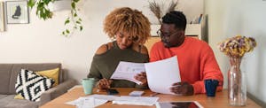 A couple sit at a table in their living room reviewing their finances to determine if they should use a 401k to pay off debt.