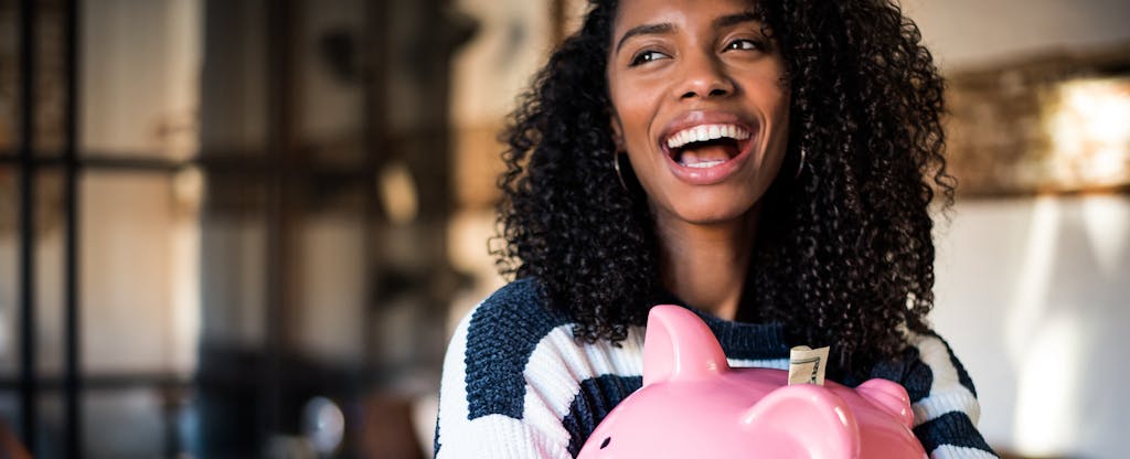 Young black woman smiling joyfully, with a large pink piggy bank in her hands