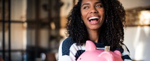 Young black woman smiling joyfully, with a large pink piggy bank in her hands