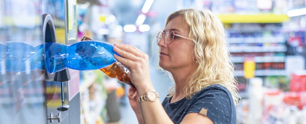 Woman in a grocery store, loading empty plastic bottles into a recycle kiosk