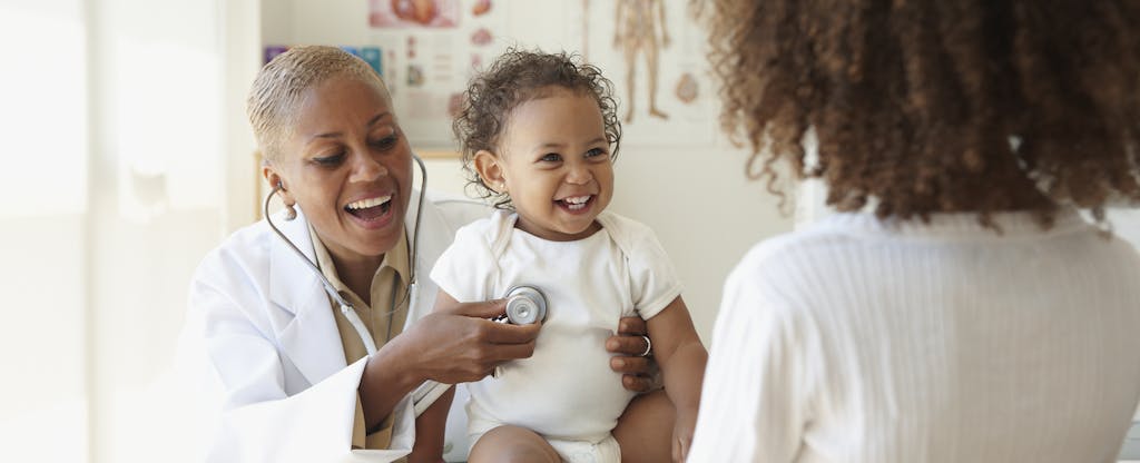Giggling baby being examined by a pediatrician, mother in the foreground