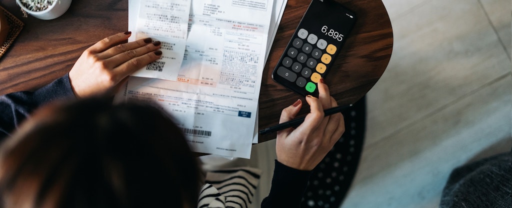 Overhead view of young Asian woman managing personal banking and finance at home. Planning budget and calculating expenses while checking her bills with calculator. Managing taxes and financial bills.