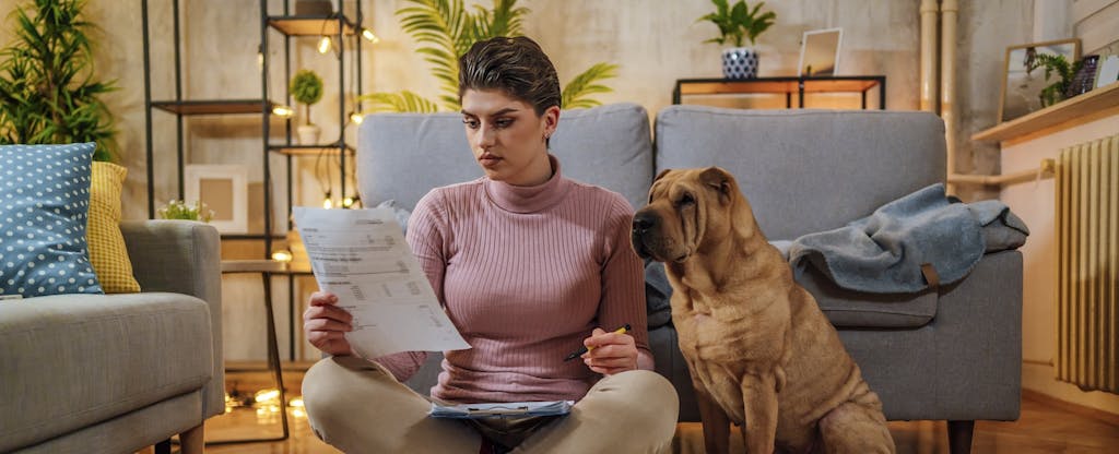 Young woman sits on the floor with her dog, looking over bills.