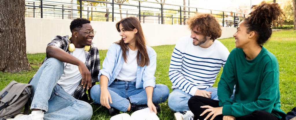 A group of students sit on a campus lawn talking and laughing.