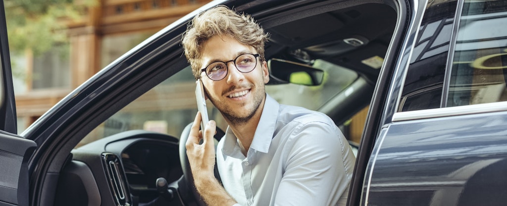 Man talking on the phone sitting in car with door open.
