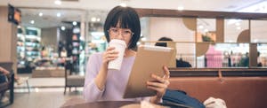 Young adult asian woman sipping coffee and using tablet at cafe.