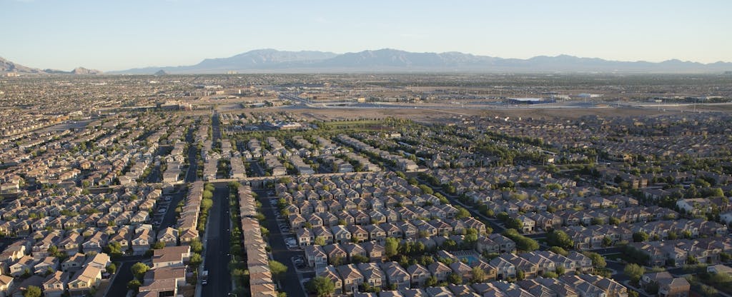 Aerial view of housing developments outside of a city, with mountains visible in the distance