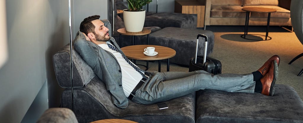 Businessperson sleeping on a grey bed in an airport lounge.