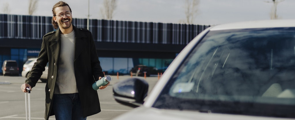 Man walking to car in airport parking lot with his luggage.