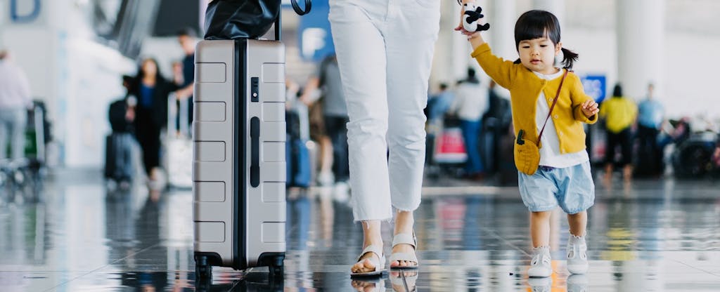 Mother holding hands with daughter while walking through airport concourse.