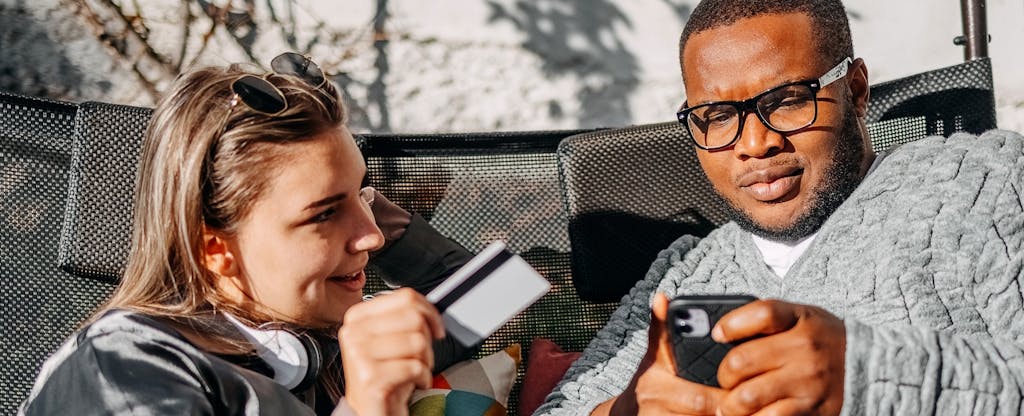 Young adult couple having fun looking at mobile phone and using credit card for online shopping at home in their back yard