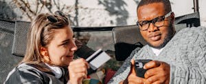 Young adult couple having fun looking at mobile phone and using credit card for online shopping at home in their back yard