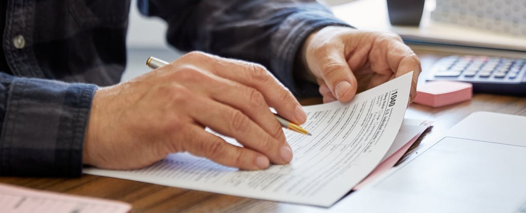 A close up photo of a person's hands as they fill out tax forms holding a pencil.