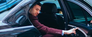 Suited businessman entering the back of a black car.