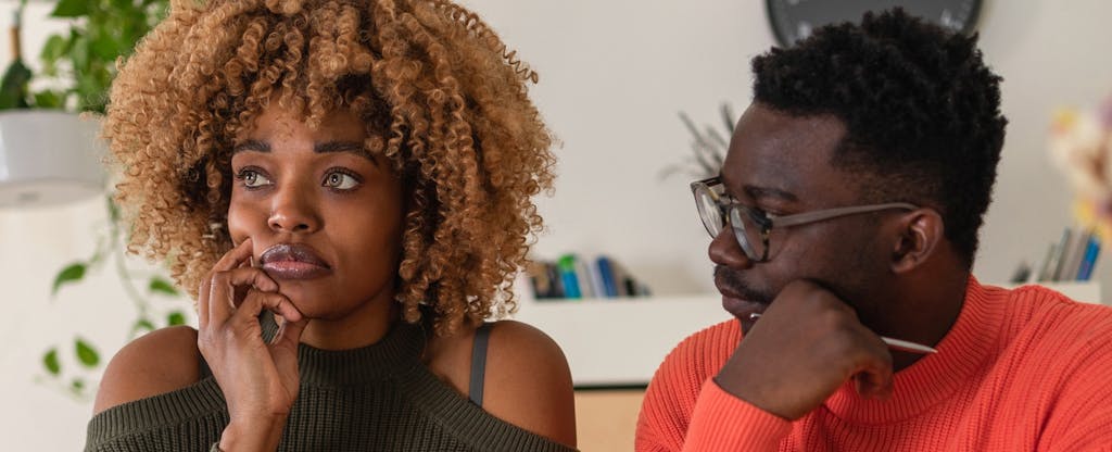 A young couple sits at the dining table and calculates their home finances. Both man and woman are staring off in thought.