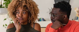 A young couple sits at the dining table and calculates their home finances. Both man and woman are staring off in thought.