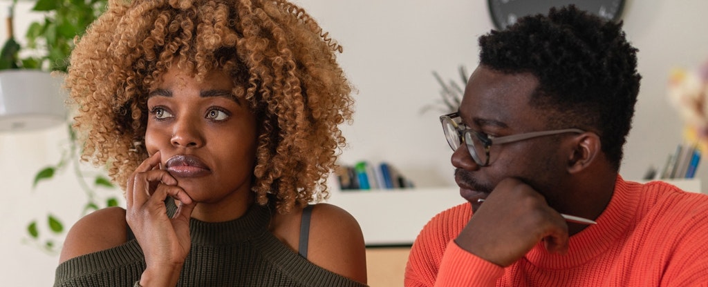 A young couple sits at the dining table and calculates their home finances. Both man and woman are staring off in thought.