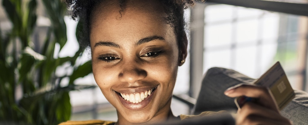 Smiling young woman on couch with credit card and laptop