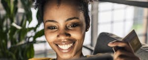 zero-percent-intro-apr-credit-cards Smiling young woman on couch with credit card and laptop